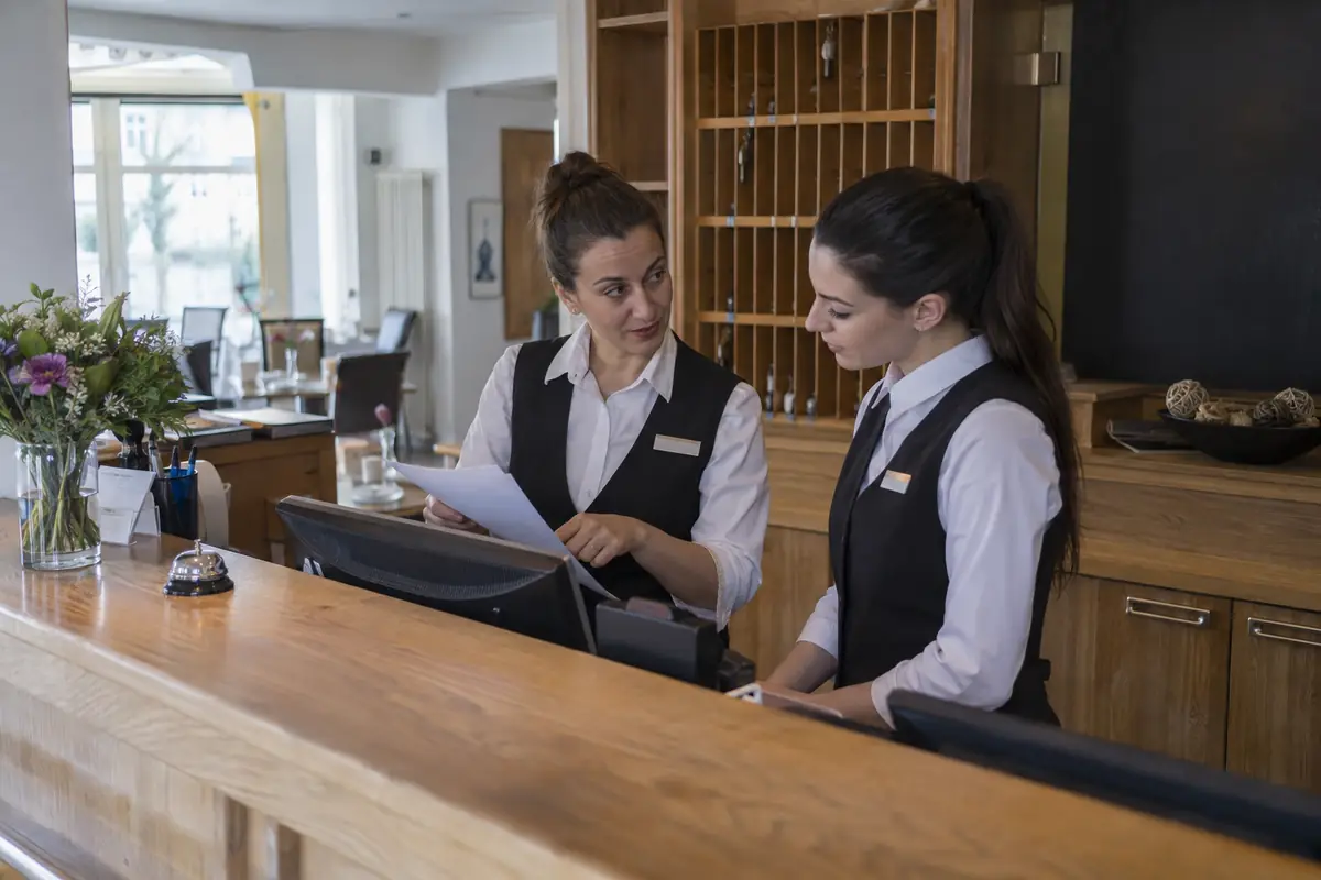Otel resepsiyonunda çalışan iki kişi misafir kaydını birlikte kontrol ediyor